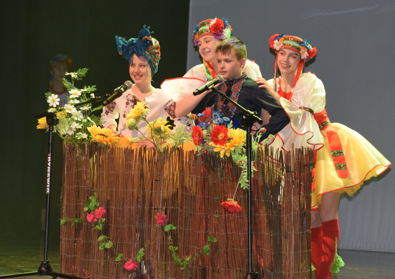 2. za płotkiem z kolorowymi kwiatami 3 uśmiechnięte dziewczynki i chłopiec w ludowych strojach ukraińskich 