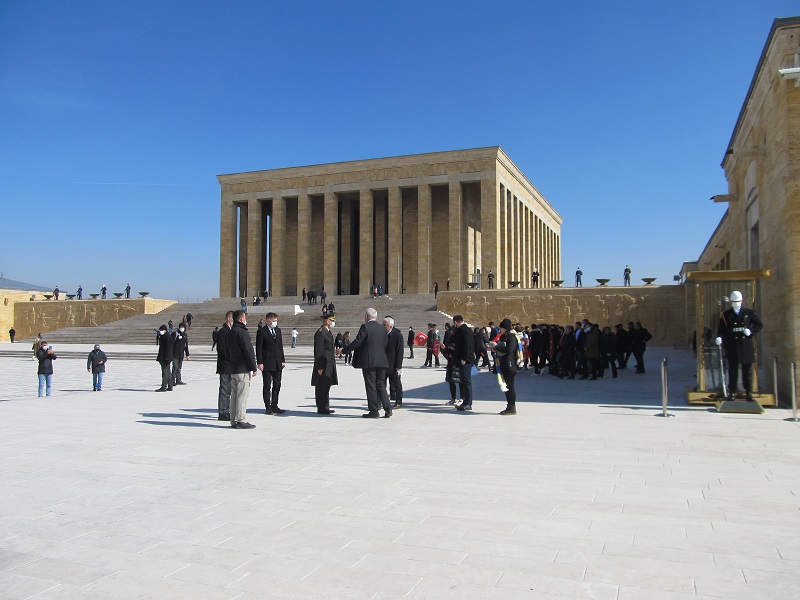 Monumentalne małzoleum Atatürka z filarami dookoła. Po obu stronach budynku stoi warta honorowa. Na placu przed nim dużo ludzi.