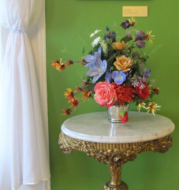 Na ozdobnym okrągłym stoliku stoi w wazonie bukiet kolorowych kwiatów.