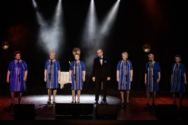 Na scenie stoi pięć pań w pięknych niebieskich sukniach i pan w garniturze.