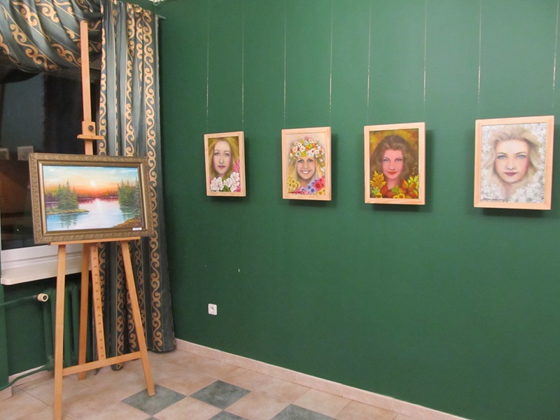 Na ścianie wiszą cztery portrety kobiet. Na staludze stoi obraz przedstawiajacy pejzaż.